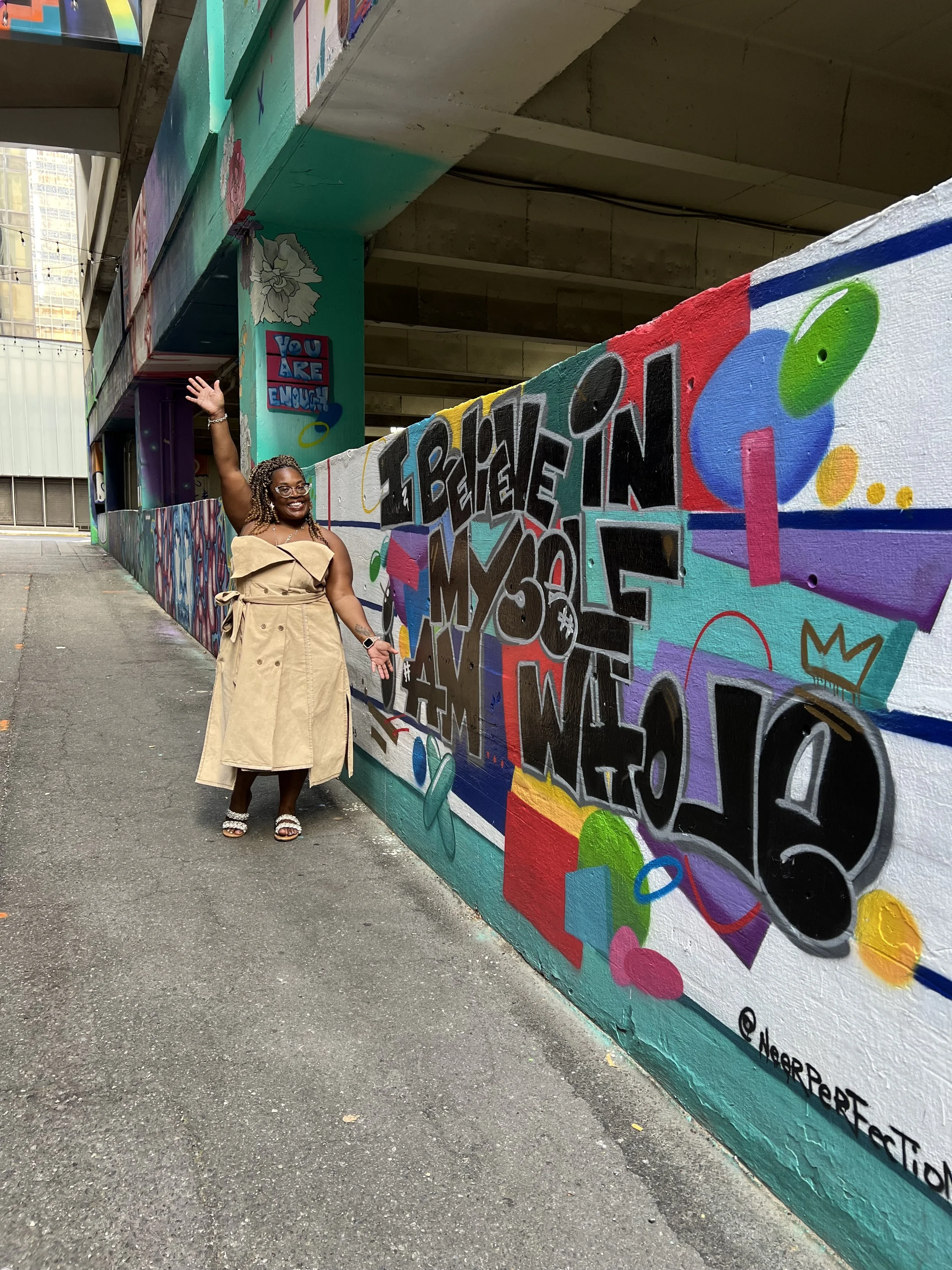 Leslie standing in front of graffiti that says "Believe in Yourself" after a Festival for Black Culture
